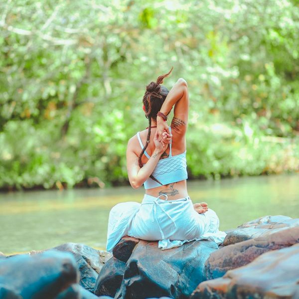 Person meditating peacefully outdoors by the water.